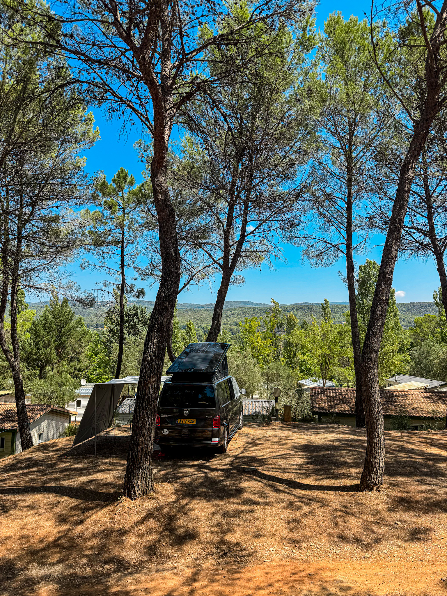 Emplacement de camping ombragé sous les pins avec vue panoramique sur les collines du Var.
