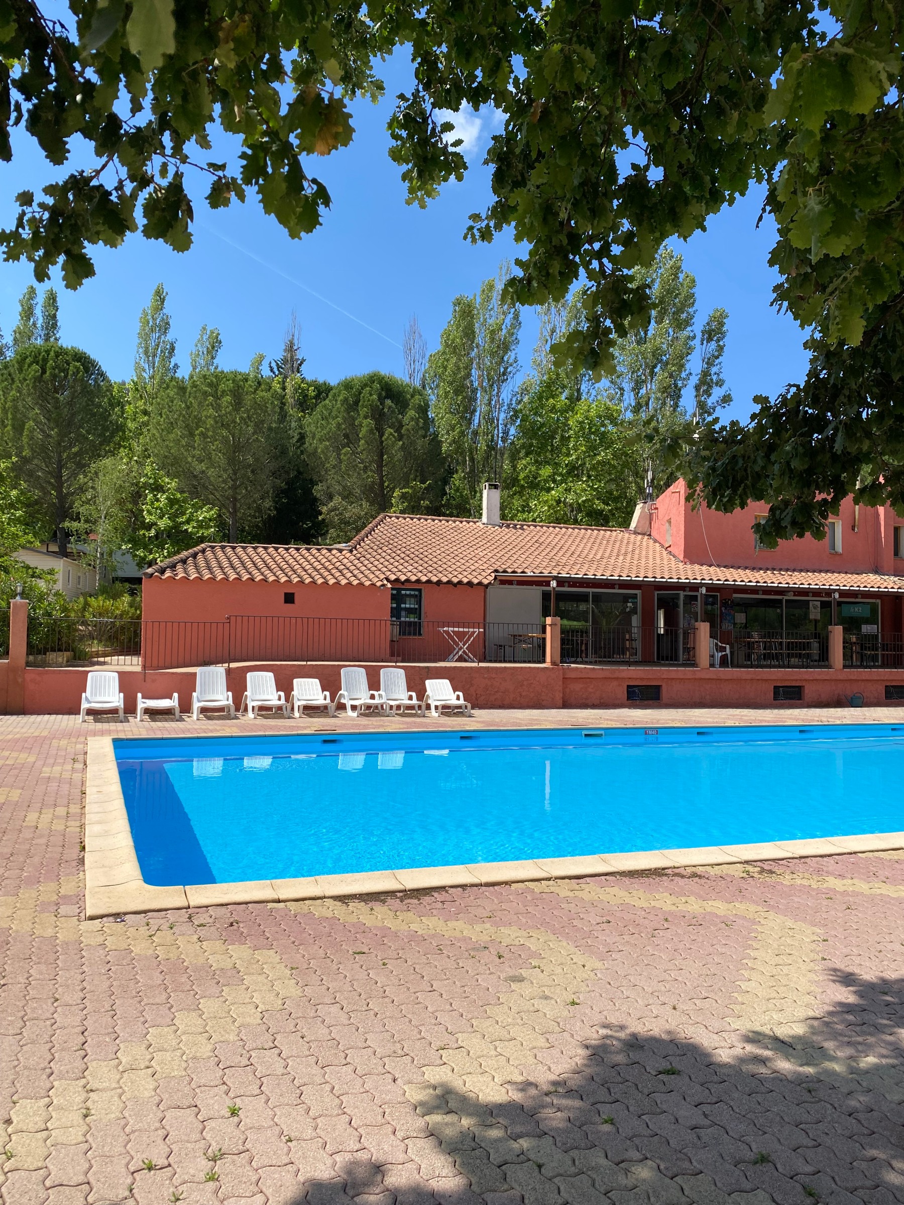 Piscine olympique avec transats en bordure et bâtiment de style provençal à Villecroze-les-Grottes.