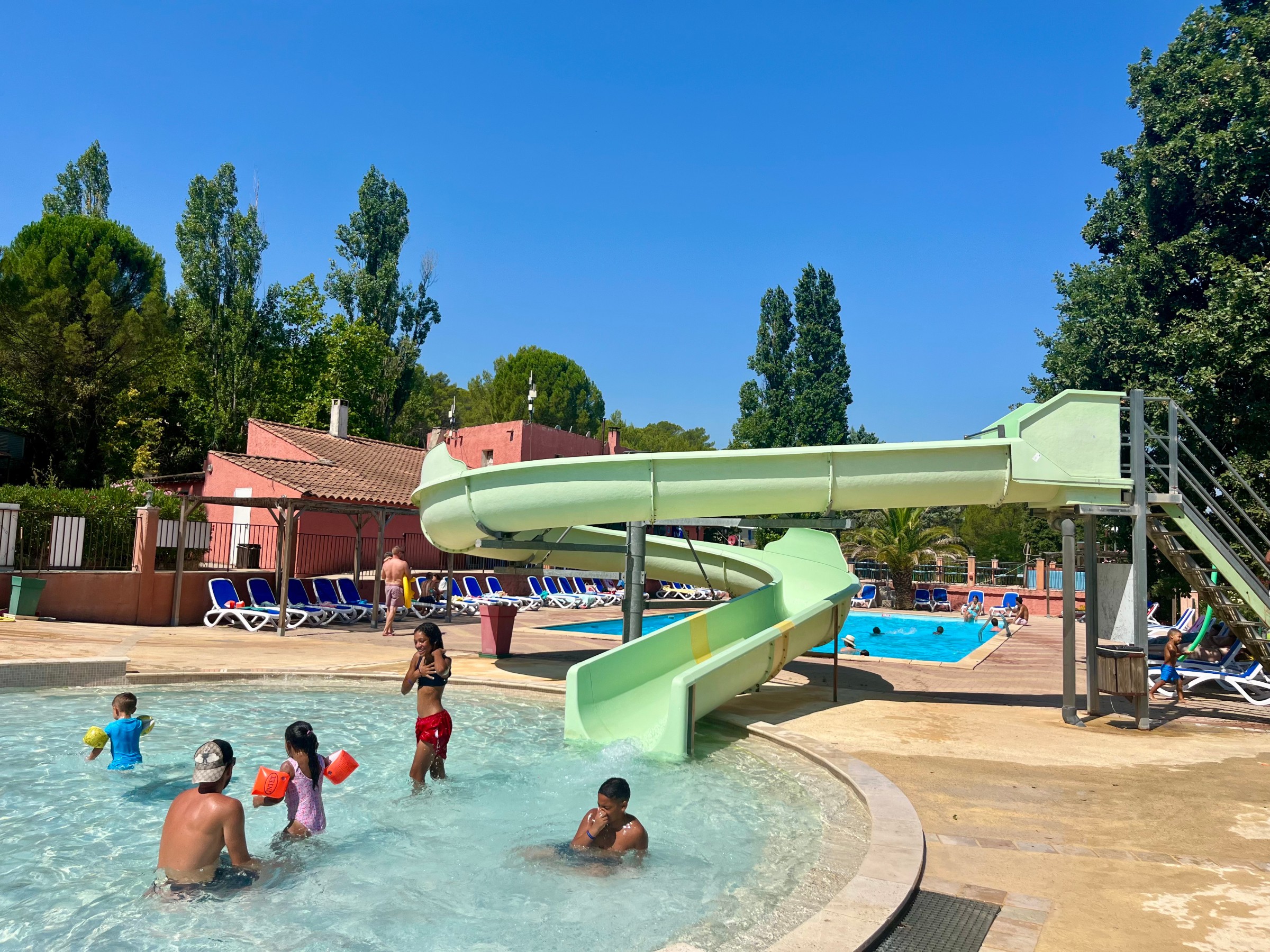 Vue d'ensemble du parc aquatique avec bassins et chaises longues au camping Les Cadenières.