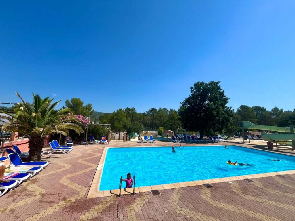 Piscine rectangulaire entourée de palmiers et transats bleus en été au Var