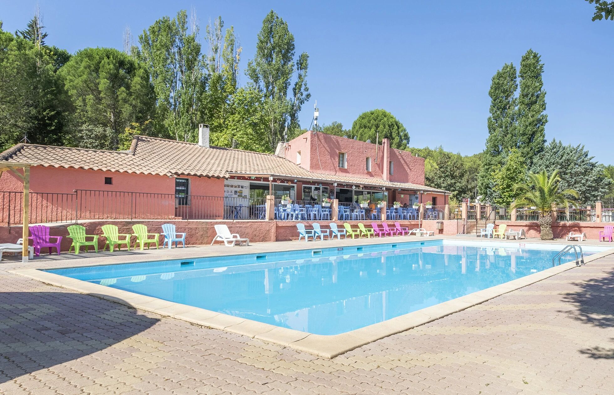 Piscine principale avec chaises longues colorées et bâtiment terracotta au Le Var